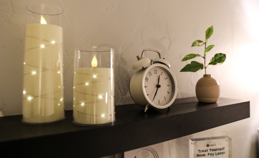 Shelf display with candles, a clock, and greenery
